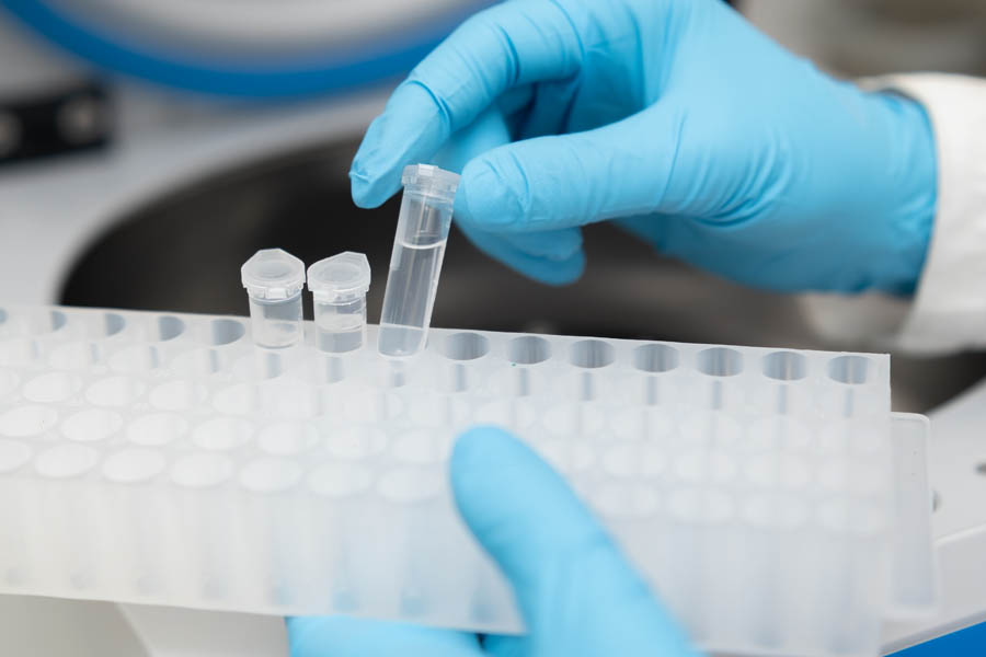 Female scientist in protective picks up samples from the centrifuge and puts into the rack